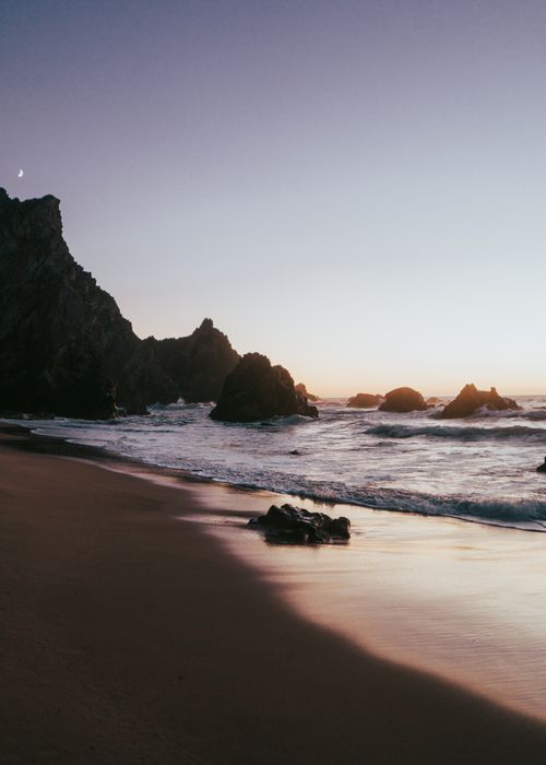 Free Tranquil seashore with waves and rock formations under a moonlit sky at sunset. Stock Photo