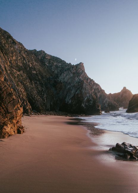 A tranquil scene of Praia da Ursa with sandy shores and rugged cliffs during sunset.