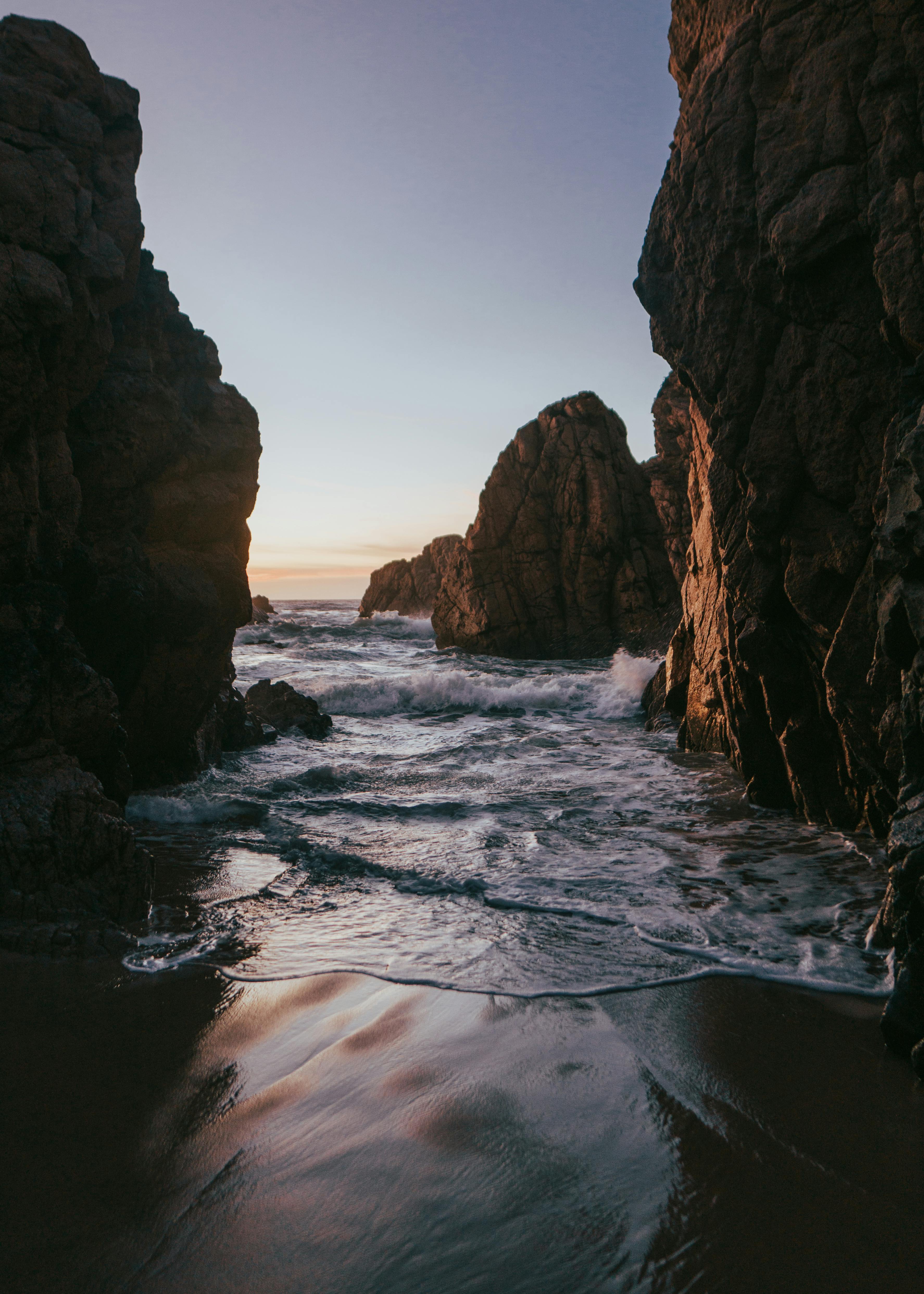 Capture of ocean waves crashing between towering rock formations at sunset.