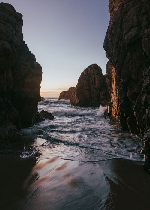 Free Capture of ocean waves crashing between towering rock formations at sunset. Stock Photo