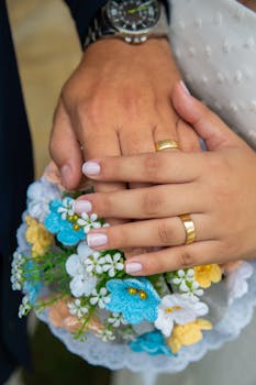 Close-up of wedding rings on a couple's hands holding a floral bouquet, symbolizing love and union.