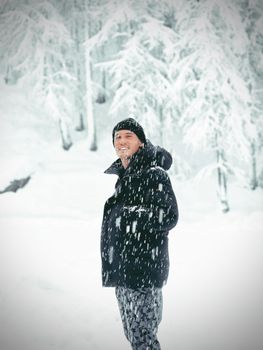 A man smiling in a snowy forest, enjoying the winter weather.
