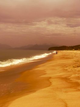 Person walking on a tranquil beach with golden hues and gentle waves at sunset.