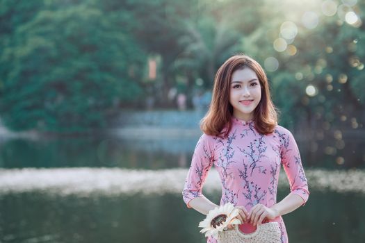 一位身着传统粉红色连衣裙的美丽亚洲女子在湖边微笑，捕捉宁静的夏日瞬间