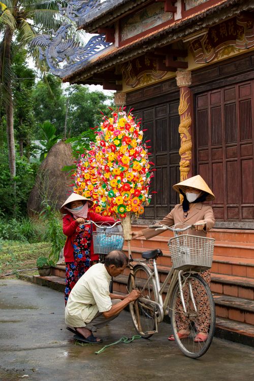 Free A man repairs a bicycle beside two women in traditional hats in Vietnam. Stock Photo