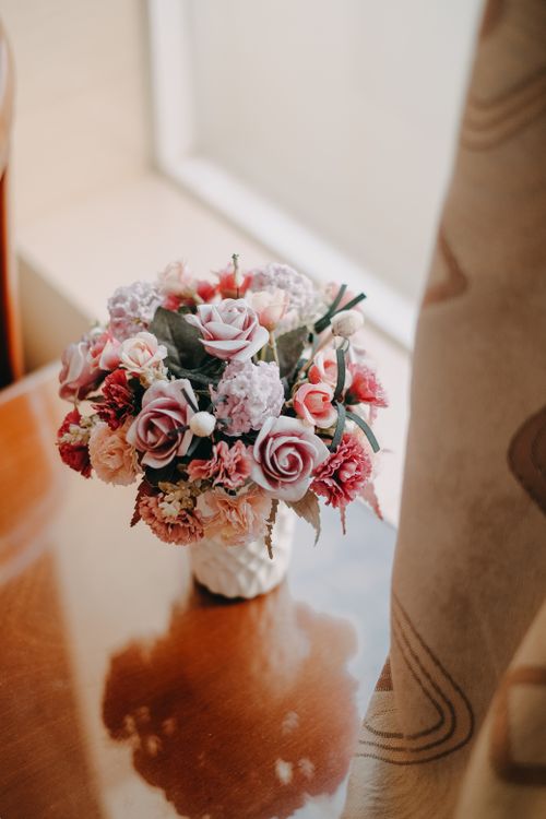 Free A beautiful bouquet of roses and carnations elegantly arranged on a wooden table beside a window. Stock Photo
