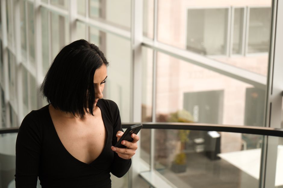 Photo by Irakli Tskipurishvili on Pexels Stylish woman in black long sleeves looking at smartphone indoors by a glass wall.