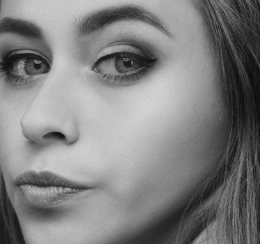 Close-up black and white portrait of a woman with striking makeup and expressive eyes.