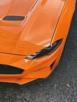 Detailed view of an orange sports car's shiny headlight and hood.