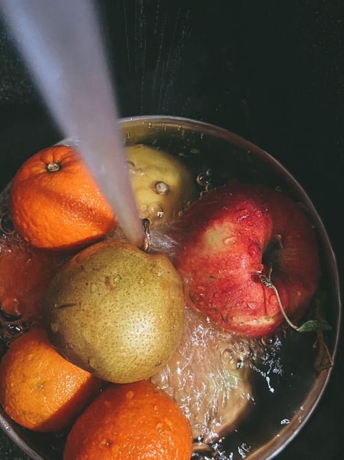 Free A vibrant assortment of fresh fruits including oranges, pears, and apples being washed in a stainless steel bowl under running water. Stock Photo