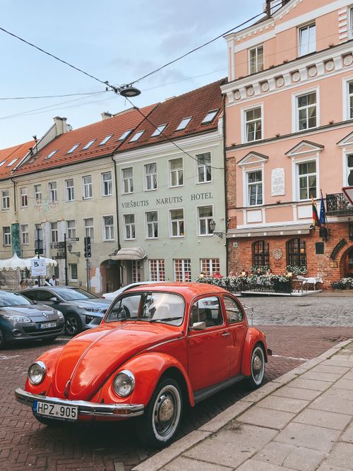 Free Red vintage car parked on a cobblestone street in a historic European town with classic architecture. Stock Photo