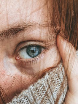 A detailed close-up of a woman's blue eye and red hair with a knitted sweater.