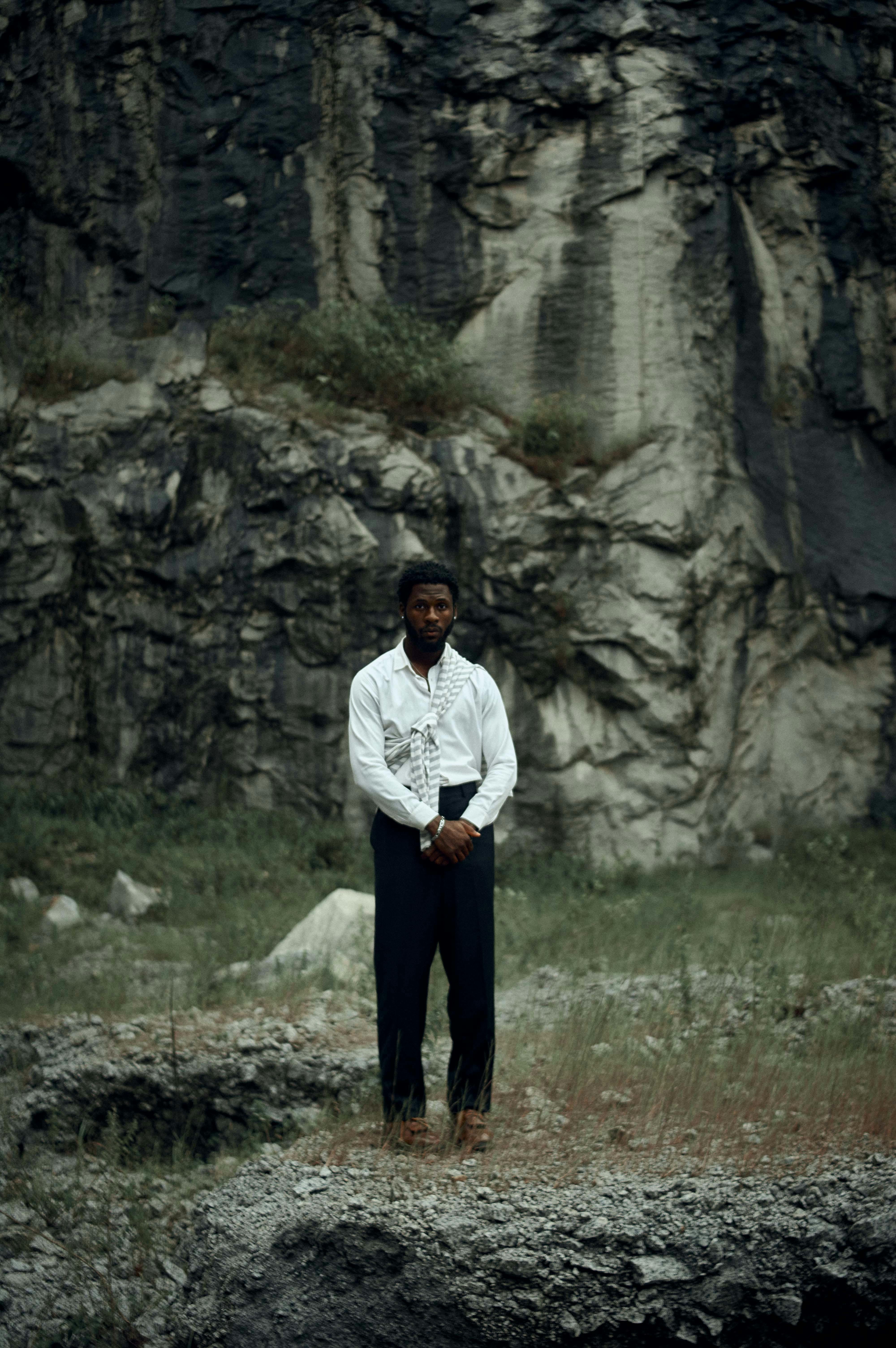 A man stands in front of a rocky cliff, showcasing nature's rugged beauty.