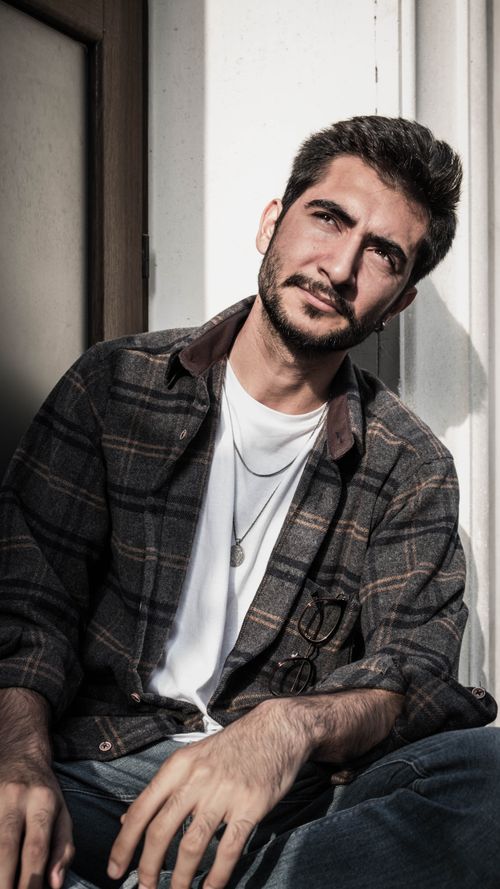 Free Portrait of a bearded man wearing a plaid shirt, sitting casually in sunlight. Stock Photo