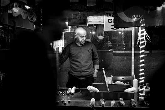 Monochrome photo of a man selling corn at a street food stall, capturing urban life.
