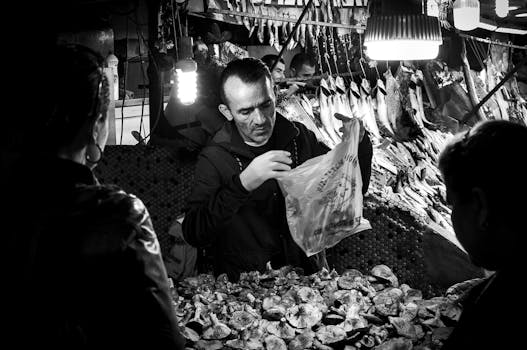 Grayscale image of a market vendor selling seafood and mushrooms at a bustling market.