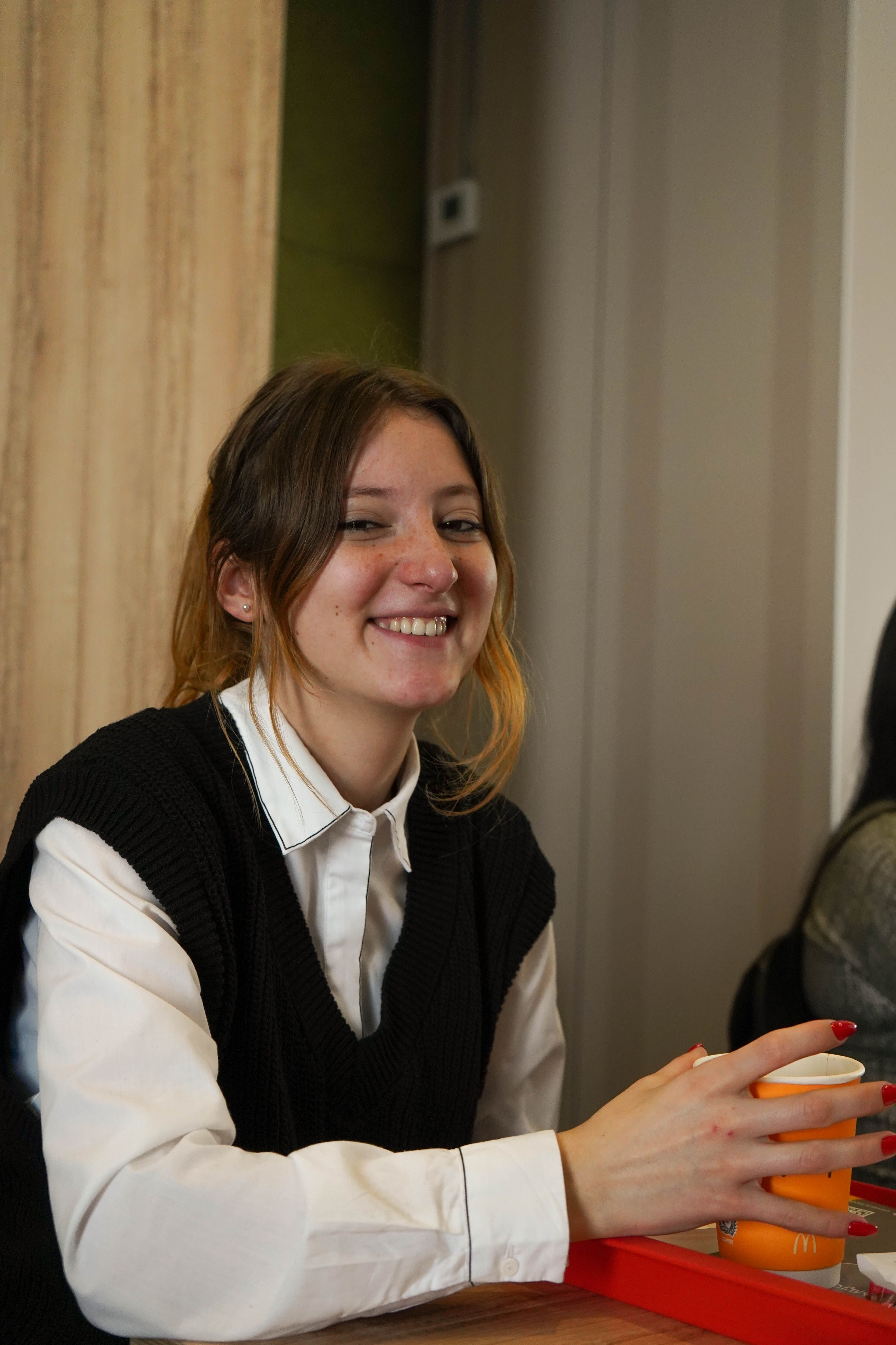 Cheerful young woman smiling and holding a drink indoors.