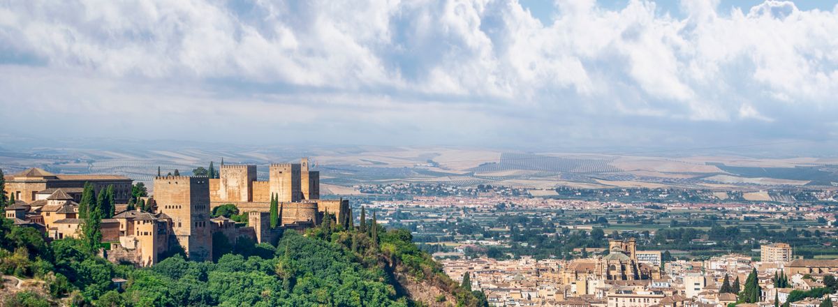 A scenic view of the historic Alhambra in Granada, Spain, surrounded by lush greenery and an expansive cityscape.