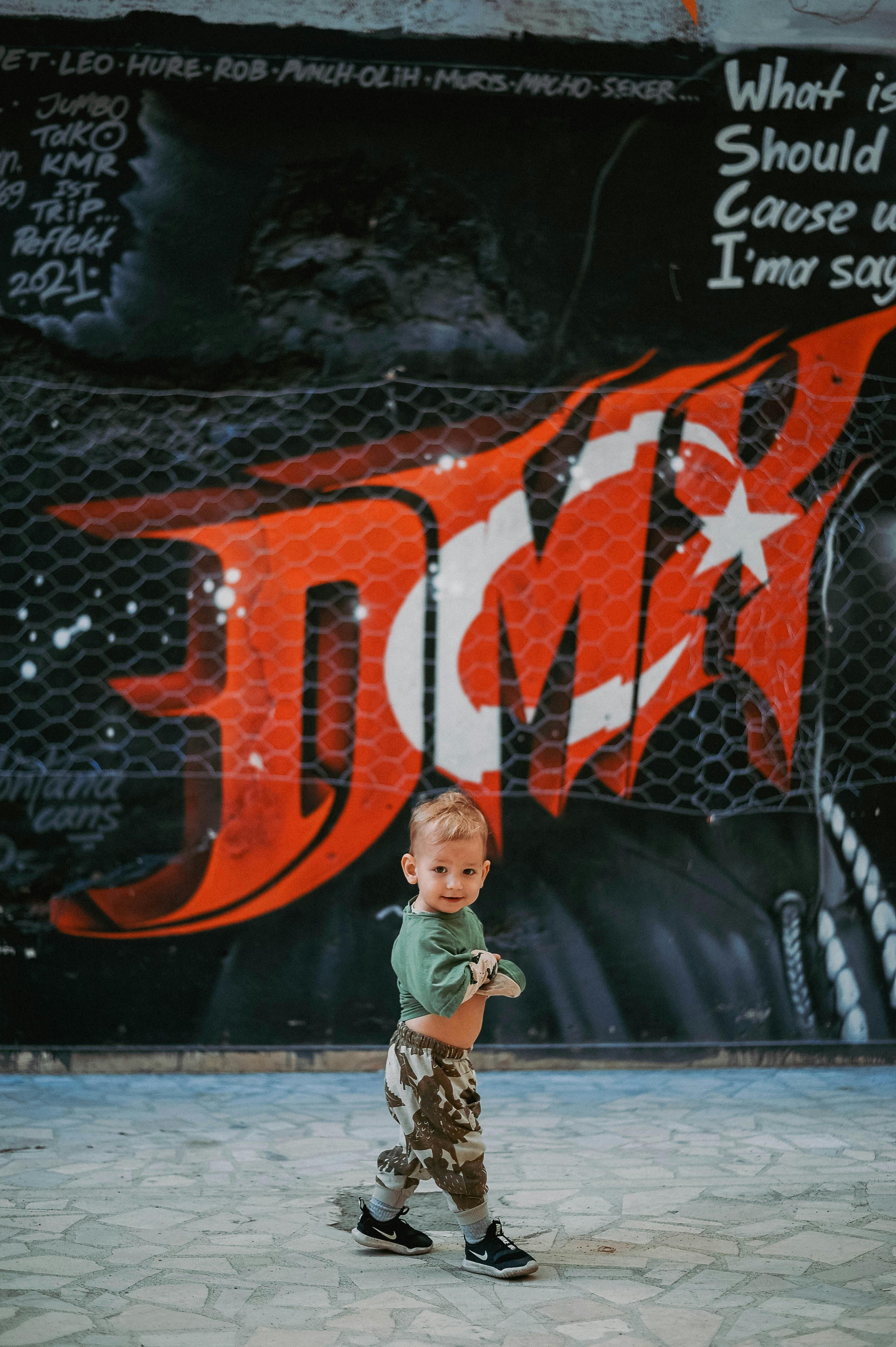 Cute toddler boy standing in front of colorful graffiti, showcasing urban style and charm.