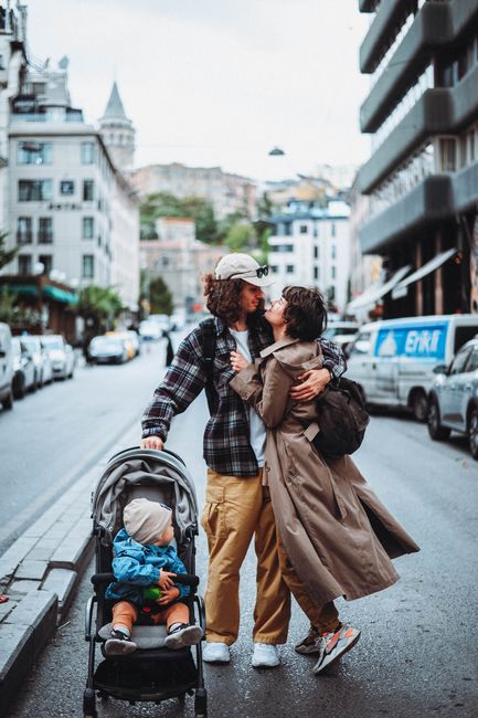 A young couple sharing an affectionate embrace on a city street, with a child in a stroller, showcasing a modern urban lifestyle.