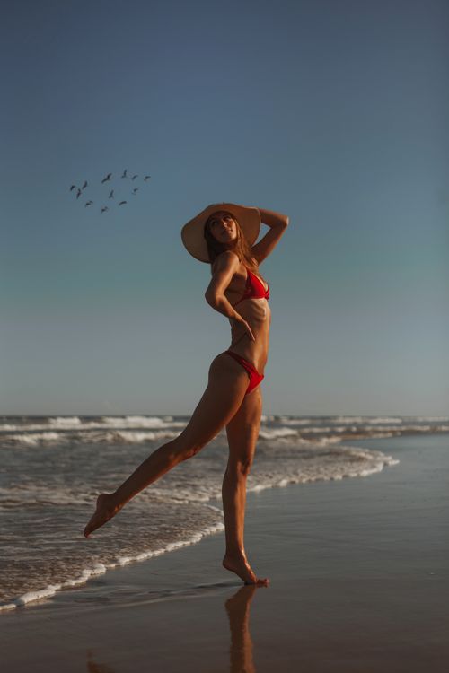 Free Woman in red bikini and straw hat posing gracefully on a sunny beach. Stock Photo