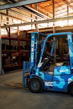 A vividly colored blue forklift parked in a well-lit, spacious warehouse with metal shelving in the background.