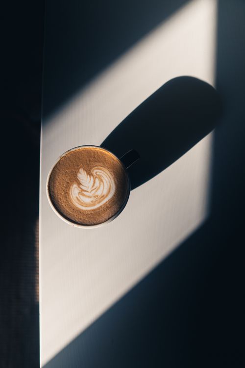 Free Stylish photo of a coffee cup with intricate latte art casting a shadow. Perfect for coffee culture themes. Stock Photo