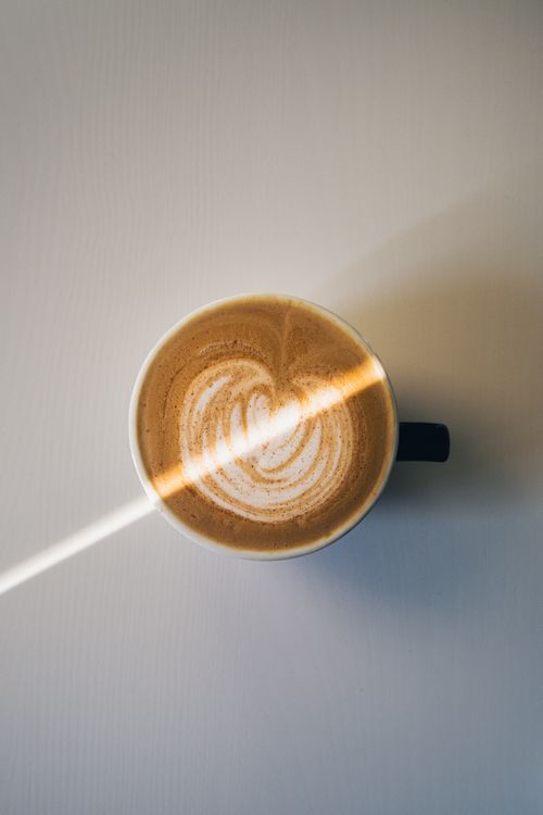 Free Overhead shot of a coffee cup with intricate latte art, illuminated by a sunbeam on a white surface. Stock Photo