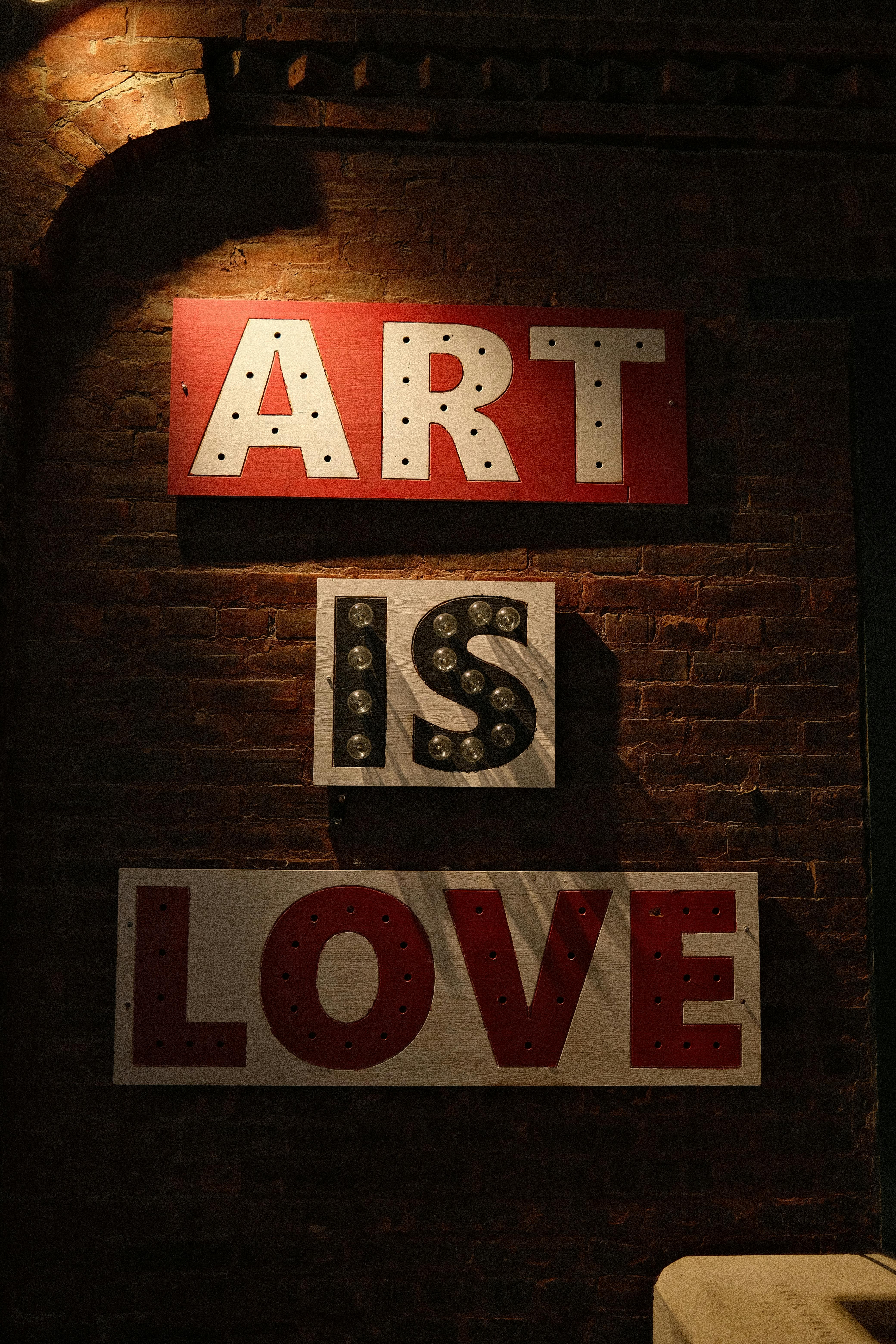 Illuminated signage with words 'Art is Love' on a brick wall, conveying creativity.