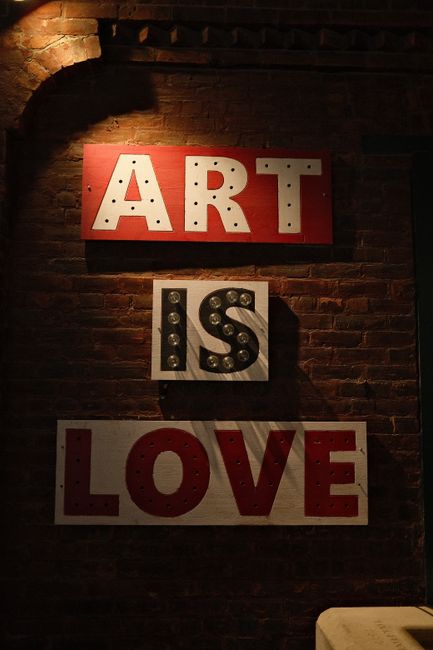 Illuminated signage with words 'Art is Love' on a brick wall, conveying creativity.