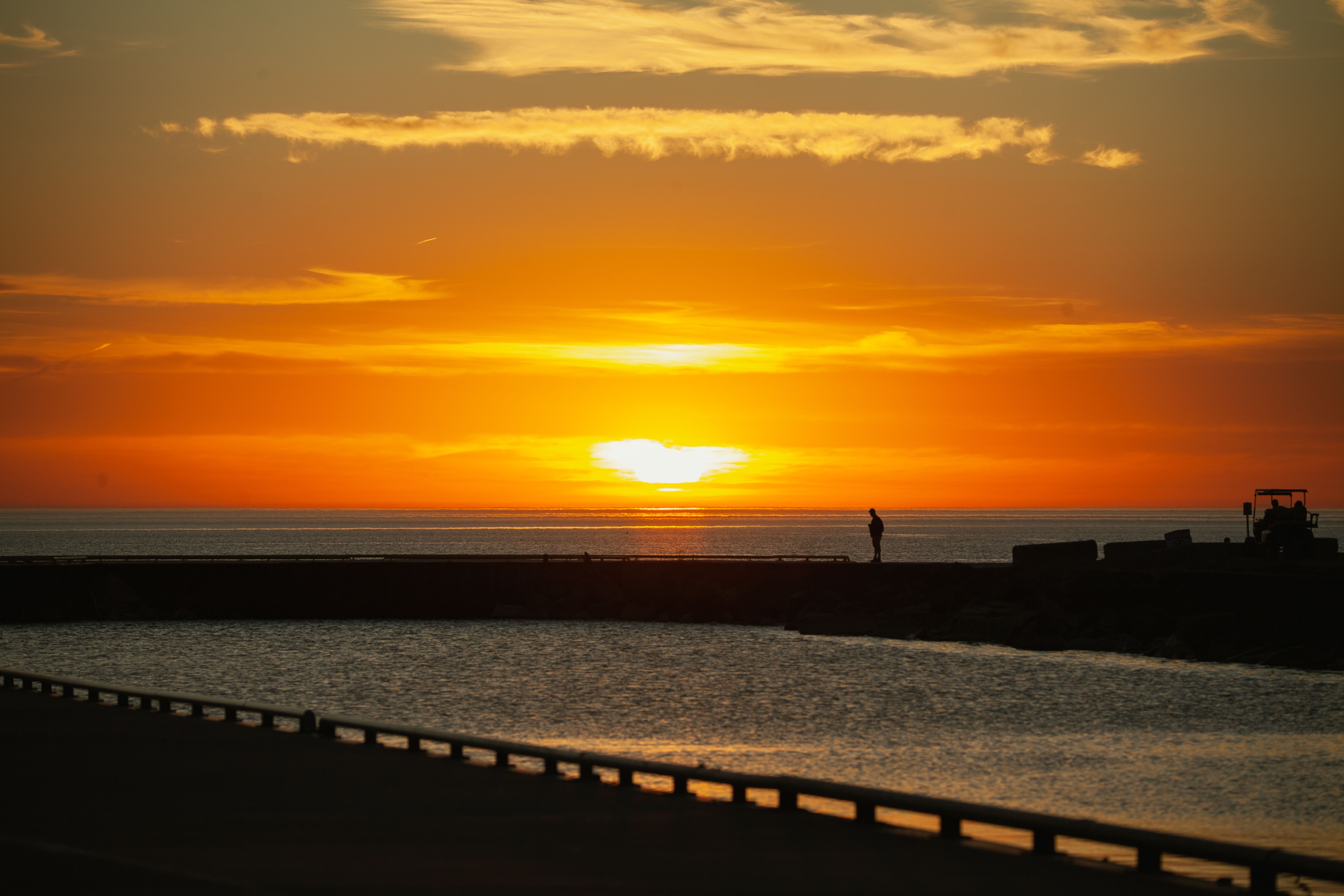 A peaceful silhouette stands against a golden sunset above a calm harbor, evoking romance and serenity.