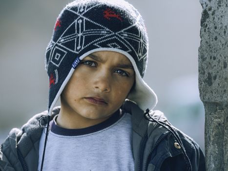 Portrait of a young boy wearing a winter hat and jacket outdoors, exuding a serious expression.