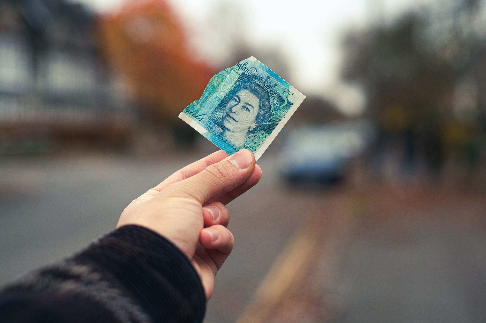 A hand holds a torn British pound note on a street in Cambridge, UK.