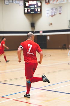 A man in a red jersey playing indoor soccer in a sports hall.