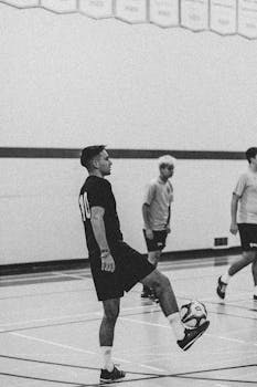 Black and white image of men playing indoor soccer, highlighting skill and teamwork.