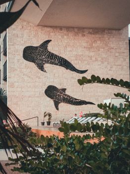 Artistic whale shark mural on a brick wall in Playa del Carmen, surrounded by lush greenery.