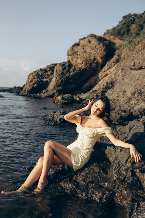 Free A woman in a sundress poses on a rocky shore by the sea in Turkey, enjoying the sunset. Stock Photo