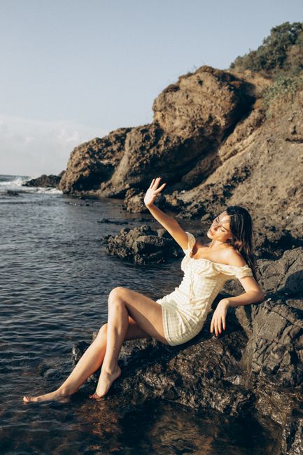 A woman in a white dress enjoys a sunny day by the rocky Turkish seaside.