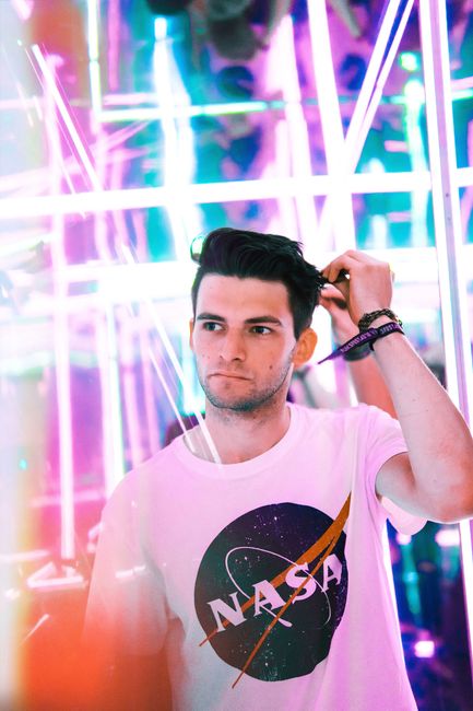 Stylish young man in a white shirt stands amidst vibrant neon lights, creating a colorful ambiance.