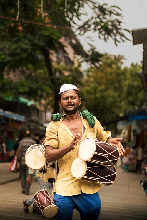 Free Street musician in Mumbai playing traditional drums with vibrant energy on a bustling outdoor alley. Stock Photo