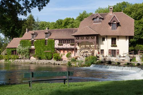 Free Picturesque historic watermill by a calm river in Gasny, Normandie, surrounded by lush greenery. Stock Photo