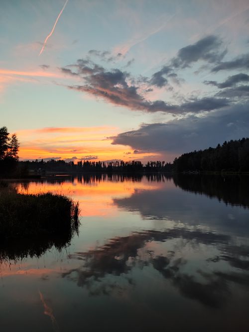 Free Stunning sunset over a tranquil lake with mirrored reflections of colorful clouds and surrounding forest. Stock Photo