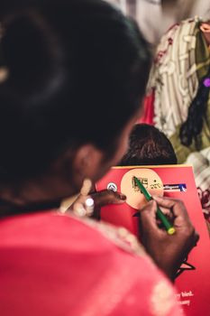 A person using a green pencil to draw on a red notebook with selective focus.