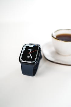 Close-up of a smartwatch and coffee cup on a white table, showcasing modern technology and lifestyle.