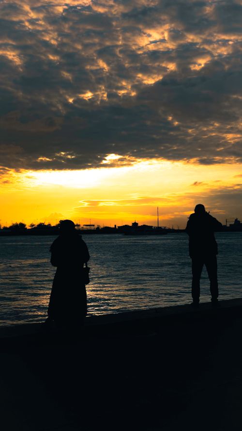 Free Silhouetted figures on Istanbul waterfront at golden hour capturing the serene sunset. Stock Photo