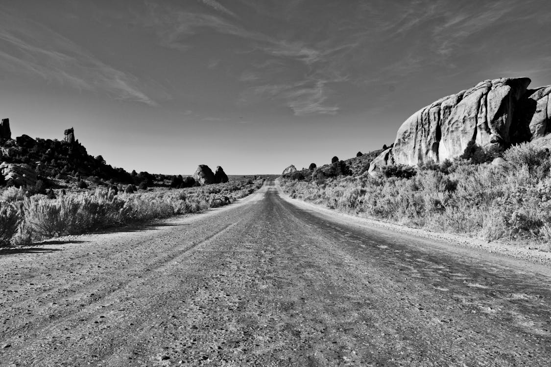 Grayscale Photography of Empty Soil Road Under Cloudy Skies