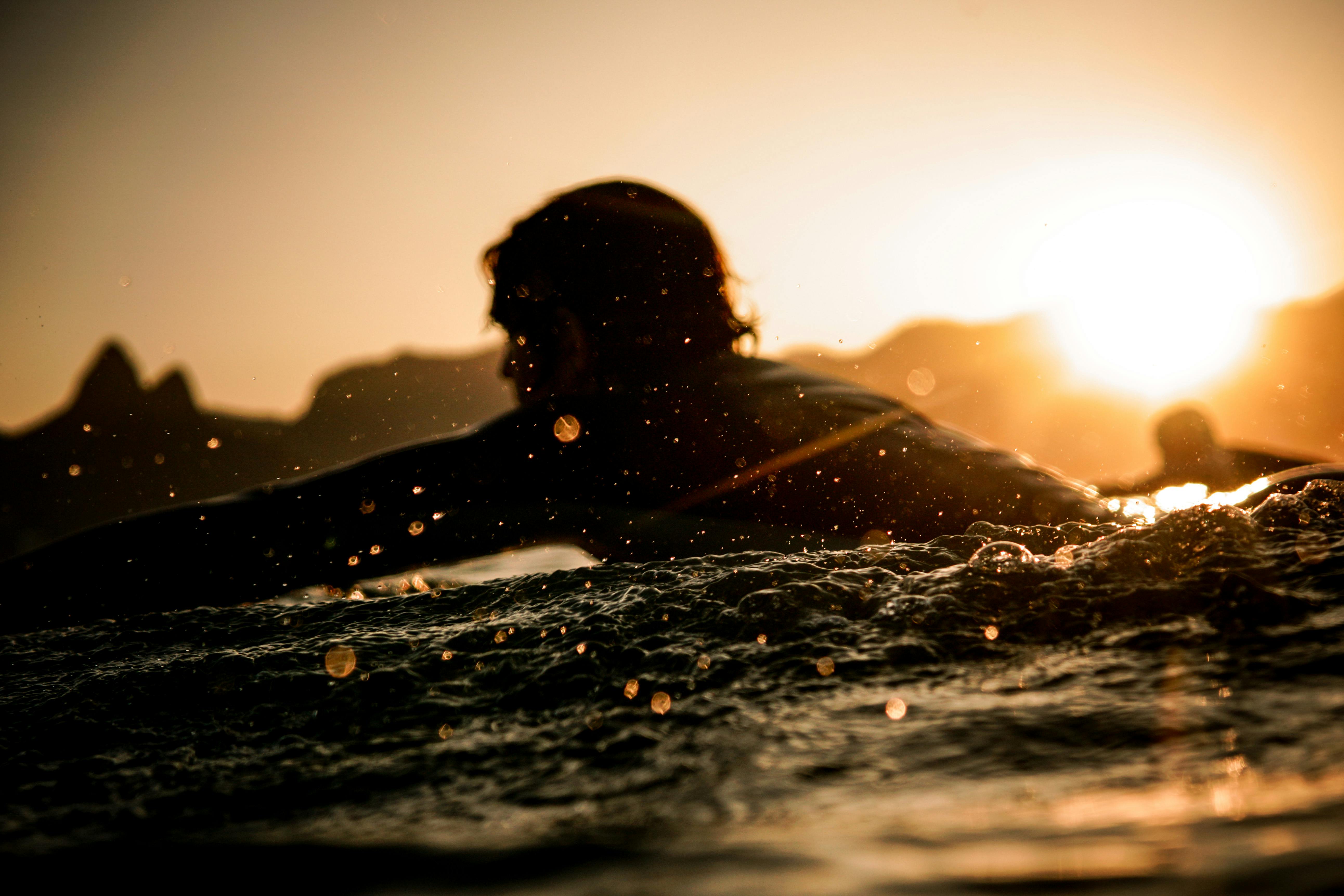 在充满活力的里约热内卢日落期间冲浪者划桨的剪影