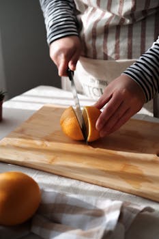 Hands slicing a juicy orange on a wooden board with natural lighting.