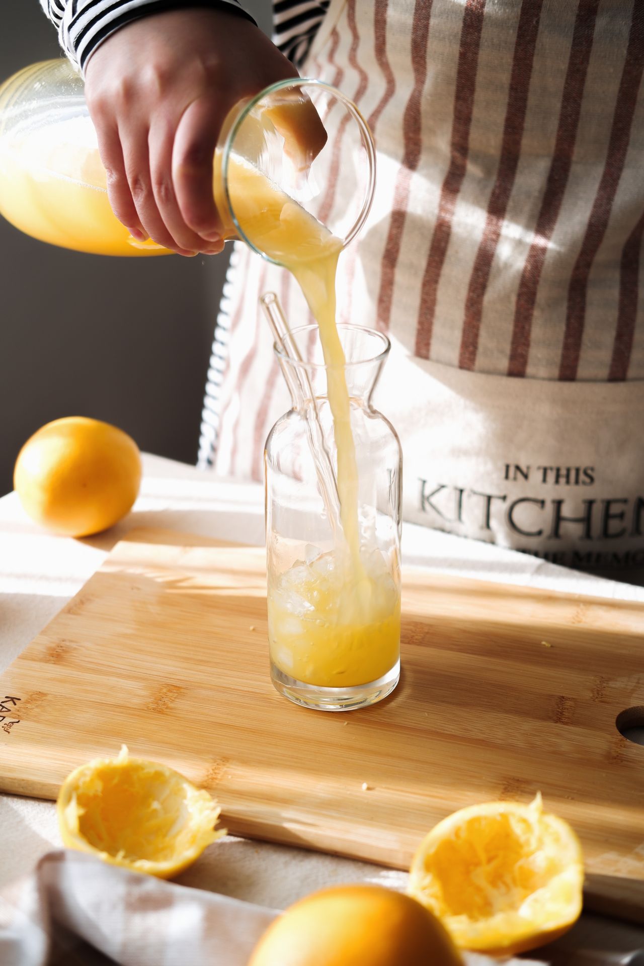 Hand pouring fresh lemonade into a glass in a sunlit rustic kitchen with wooden cutting board.