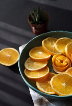 Close-up of freshly sliced oranges arranged in a blue bowl with a decorative rose shape.